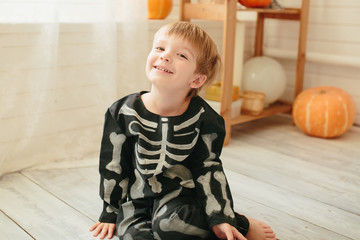 Little cute boy in a skeleton costume is ready for the celebration of Halloween in the room with the scenery for Halloween.