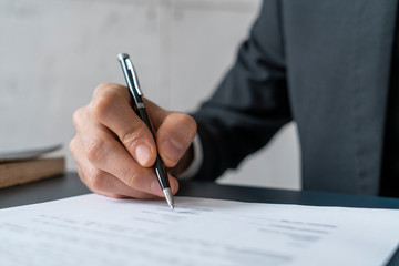 Close up of hand of young businessman signing contract at blurred office table. Concept of employment and management