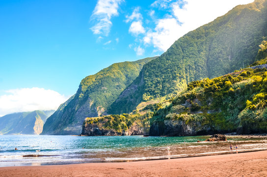 Beautiful sandy beach in Seixal, Madeira Island, Portugal. Green hills covered by tropical forest in the background. People on the beach. Summer vacation destination. Portuguese landscape