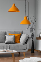 Orange lamp above grey scandinavian sofa in modern interior