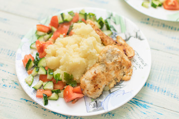 Mashed potatoes with chop and fresh vegetable salad in a plate on wooden background.