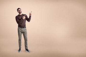 Fototapeta na wymiar Young smiling man wearing casual clothes and pointing up on beige background