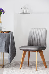 Stylish chair next to dining table with grey tablecloth in trendy dining room interior