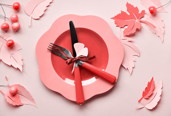 Table setup for Autumn celebration, coral color toned image. Plastic plate on paper with paper Autumn leaves