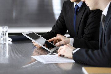 Businessman using tablet computer and work together with his colleague or partner at the glass desk in modern office, close-up. Unknown business people at meeting. Teamwork and partnership concept