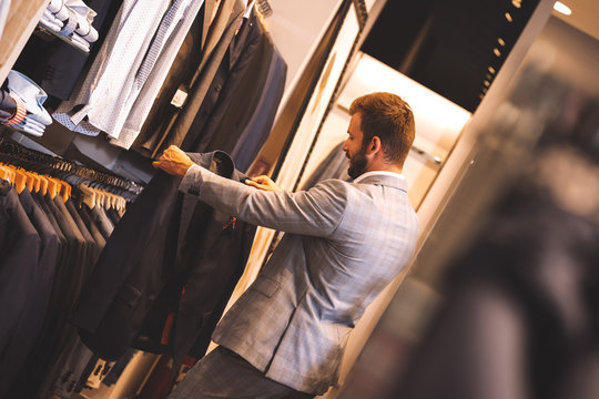 Young man choosing suit in clothes store.