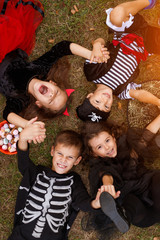 Happy kids in Halloween costumes lying on grass