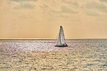 A yacht with a white sail on a smooth surface of the sea before sunset
