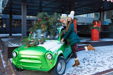 Obraz premium Beautiful woman with New Year decorations and balls on background of green retro car.Christmas and New Year holidays.