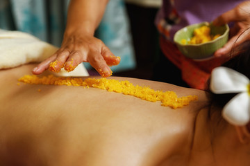 Close up of Spa therapist applying scrub salt on young woman back at salon spa. Hands massaging female back with scrub.