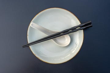 Empty plate, spoon and chopsticks on black table in asian restaurant, close up