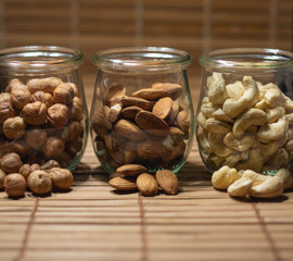 Hazelnuts, almond and cashew nuts in glass jar on brown background