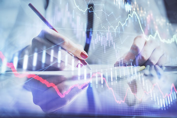 A woman hands writing information about stock market in notepad. Forex chart holograms in front. Concept of research.
