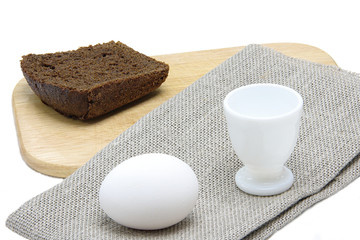 Egg, rough cloth and rye bread on a board on a white background