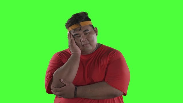 Thoughtful overweight young man standing in the studio while thinking something. Shot in 4k resolution with green screen background