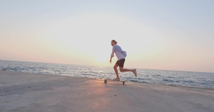 Young handsome male ride on the skateboard , sea and sunset on background , 4k UHD 