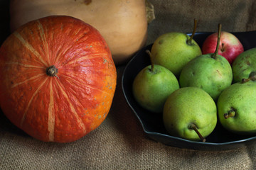 Still life orange yellow pumpkins butternut squash and red green pears, autumn farm harvest on retro canvas and black plate. Autumn fall atmospheric dark harvest still life on black background