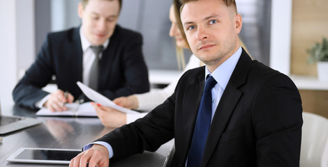 Businessman headshot at meeting in modern office. Unknown entrepreneur sitting with colleagues at the background. Teamwork and partnership concept