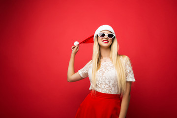 Happy blonde in santa hat on red isolated background. White rimmed sunglasses.