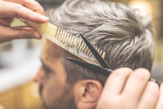 Barber cutting and modeling hair with scissors and comb.