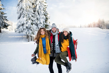 A group of cheerful young friends standing outdoors in snow in winter forest.