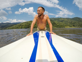 Young man paddles on a long-board in lake.