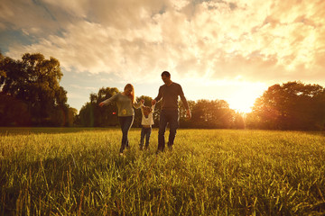 Happy family walks on the park at sunset.