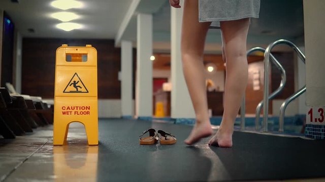 Woman putting on her shoes next to slippery floor sign in empty pool