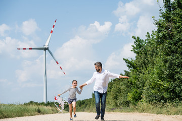 Mature father with small daughter on field on wind farm, running.