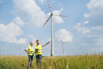 Engineers standing on wind farm, making notes.
