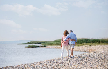 Rear view of senior couple on a holiday on a walk by the lake, walking.