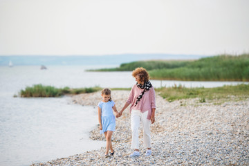 Small girl with grandmother on a holiday by the lake, walking and talking.