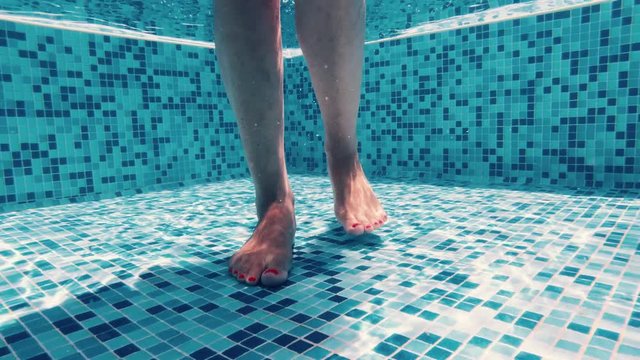 Woman&rsquo;s legs walking on the bottom of a pool, underwater