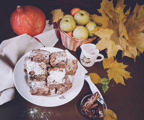 Festive apple pie with powdered sugar close-up with autumn leaves and pumpkin on the table.