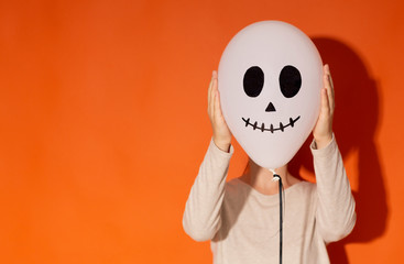 Woman hiding her face beside balloon with face on orange