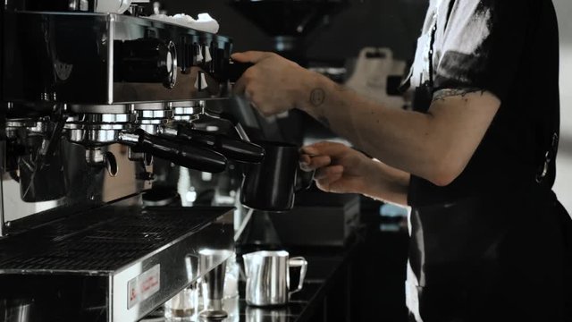 Barista at work. Steaming milk for coffee in coffee shop. Morning sun.