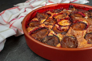 Original plum torte NYT's recipe. Homemade pie with halves of fresh plums in ceramic shape.