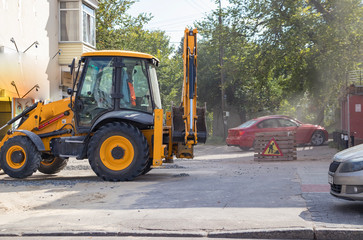 Orange excavator on wheels works in the city
