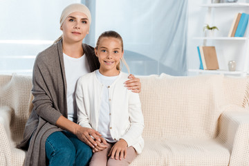 sick mother sitting on sofa with happy daughter