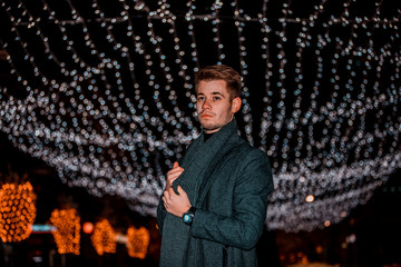 Young man in a coat with winter nigh lights in background