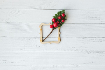 Naklejka na ściany i meble Christmas background with decorative composition of wooden frame and branch with red berries on white wooden board. Happy new year. Card. Copy space.