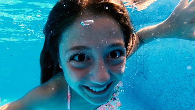 Happy girl making silly faces to the camera in pool, underwater