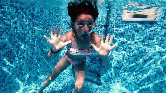 Slow motion of little girl making grimaces underwater in a pool