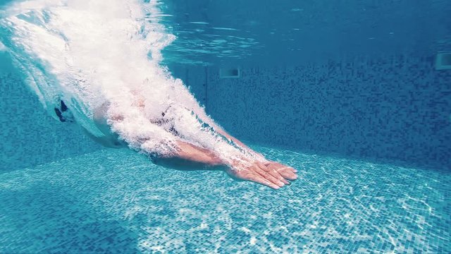 Underwater view of men jumping in the pool, slow motion