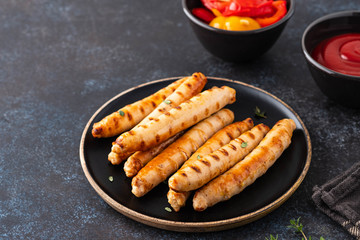 Grilled sausages on black plate with tomato sauce and thyme. Copy space.