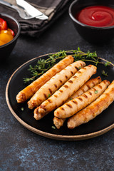 Grilled sausages on black plate with tomato sauce and thyme. Copy space.