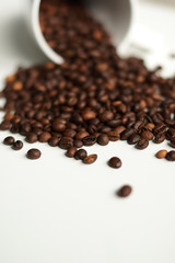 Coffee beans on a white background are beautifully scattered from a white cup.