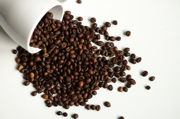 A scattering of aromatic coffee on a white background with a cup.