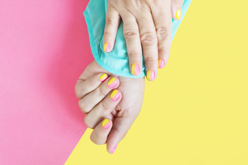 Fototapeta premium Female hands in a blue blouse with a bright pink-yellow manicure on a yellow-pink background...