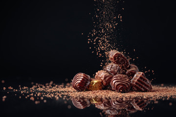 Chocolate candies on a black background sprinkled with chocolate chips. - obrazy, fototapety, plakaty